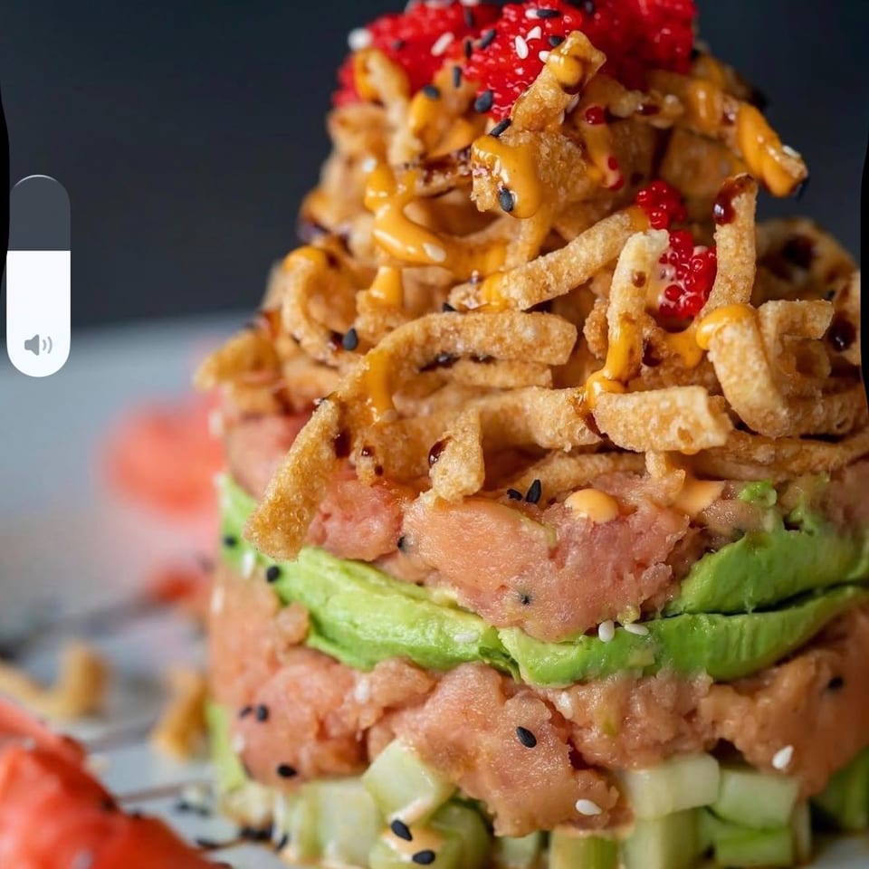 Close-up of a stacked tuna tartare with avocado, crispy noodles, and red roe.