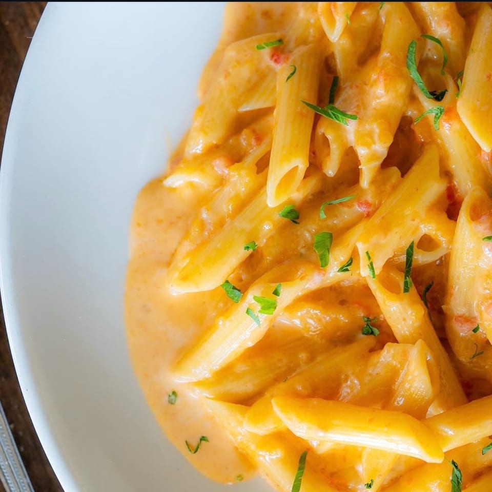 Close-up of penne pasta in a creamy orange sauce, garnished with fresh green herbs.