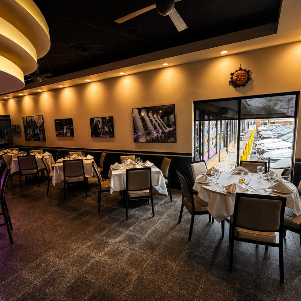 Elegant restaurant interior with set tables, warm lighting, wall art, and a view of a parking lot.