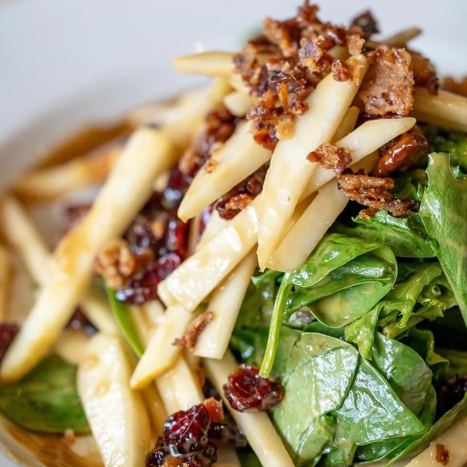 Close-up of a salad with spinach, sliced pears, dried cranberries, and crispy bacon bits.
