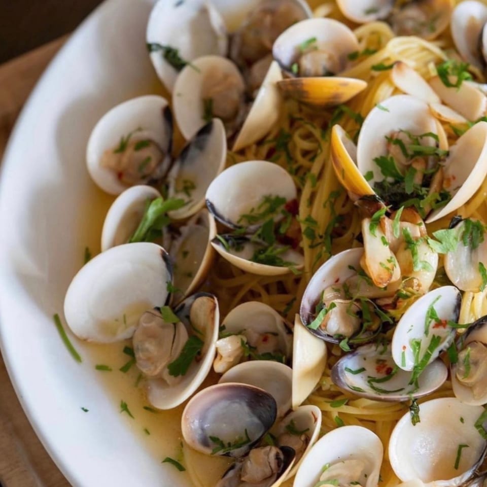 Close-up of linguine pasta with clams, garlic, and parsley in a white bowl.
